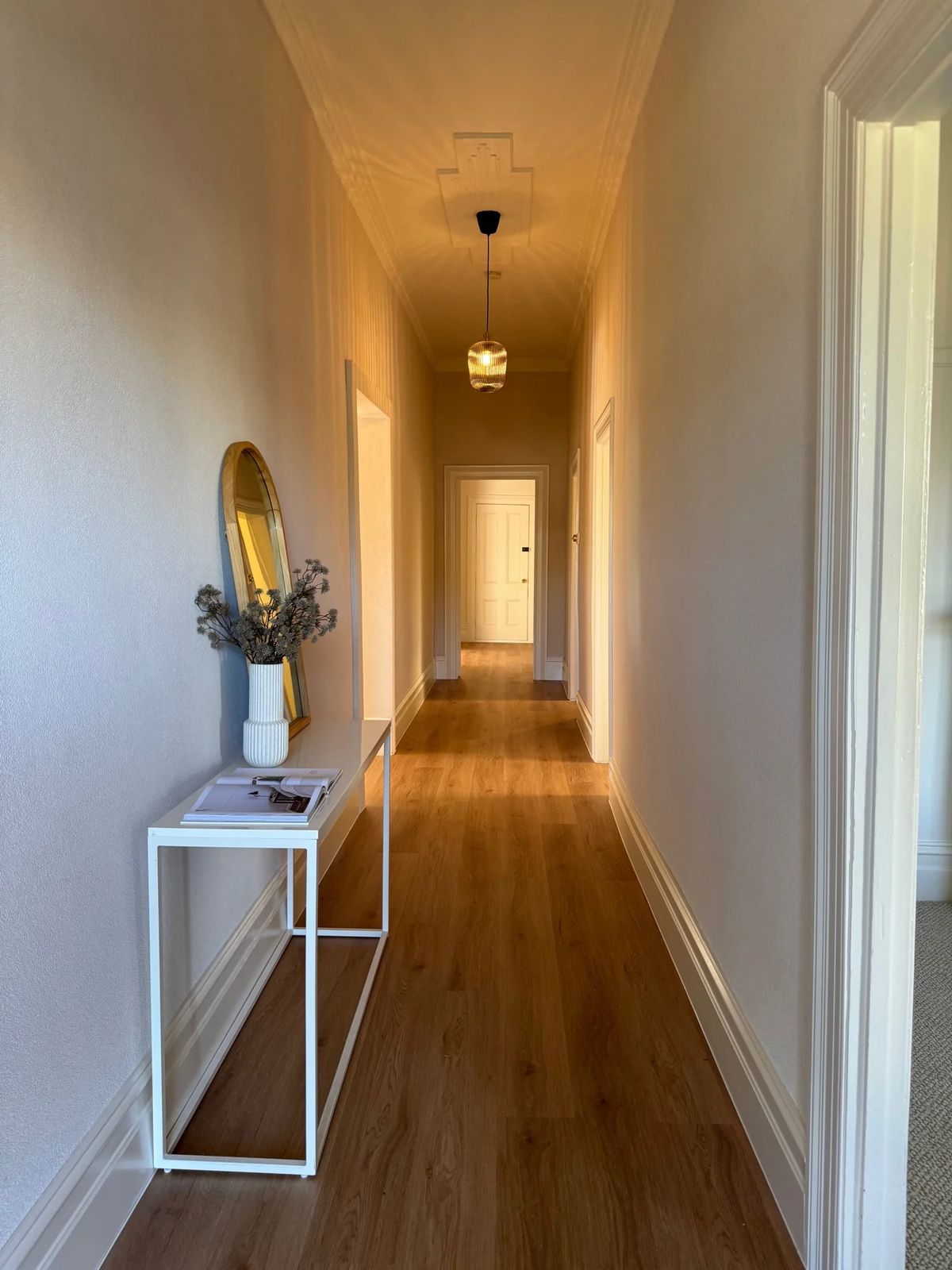 The same hallway after: white walls, new timber floors and a pendant light