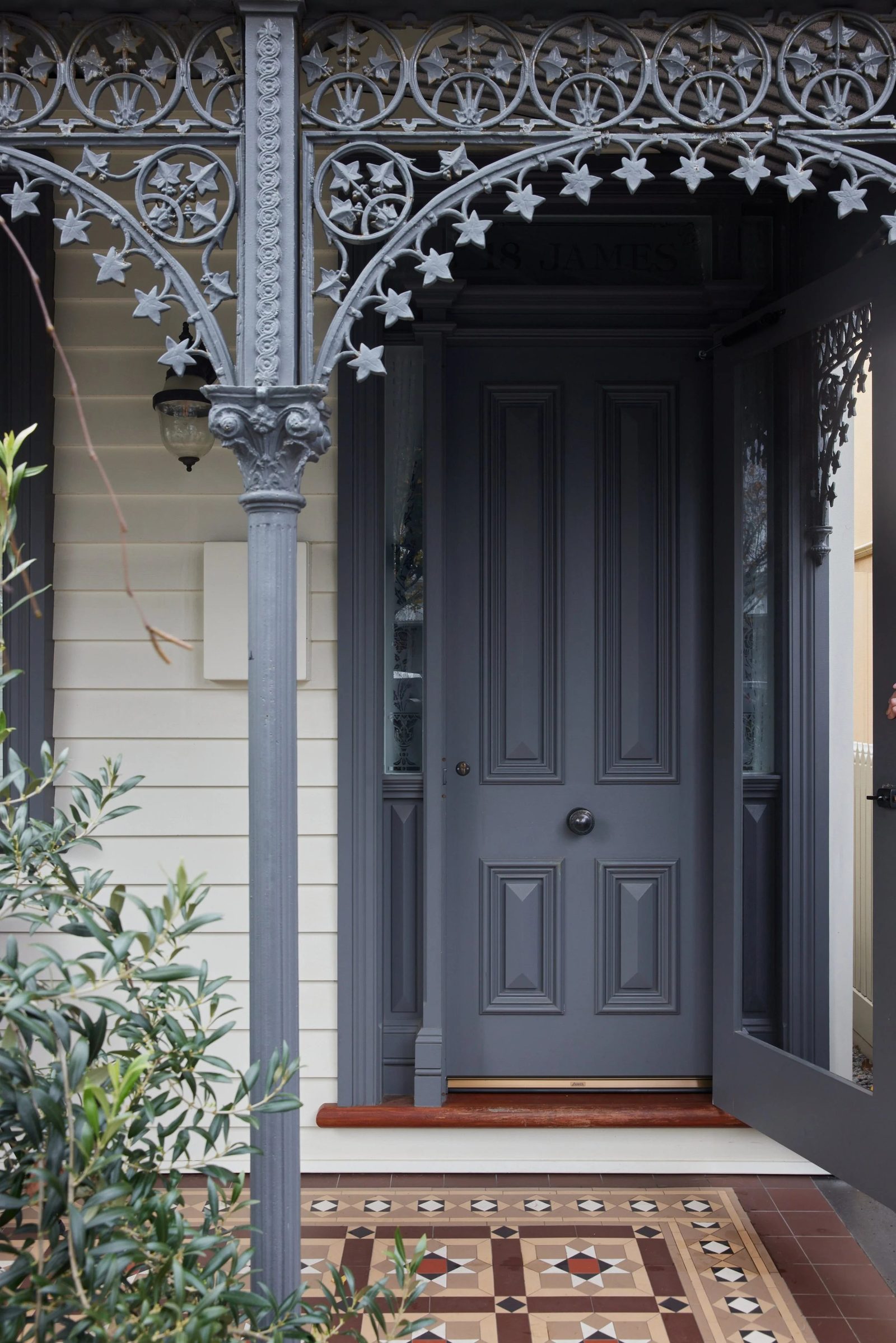 Restored heritage front door in deep blue with iron lacework and a tessellated tile path