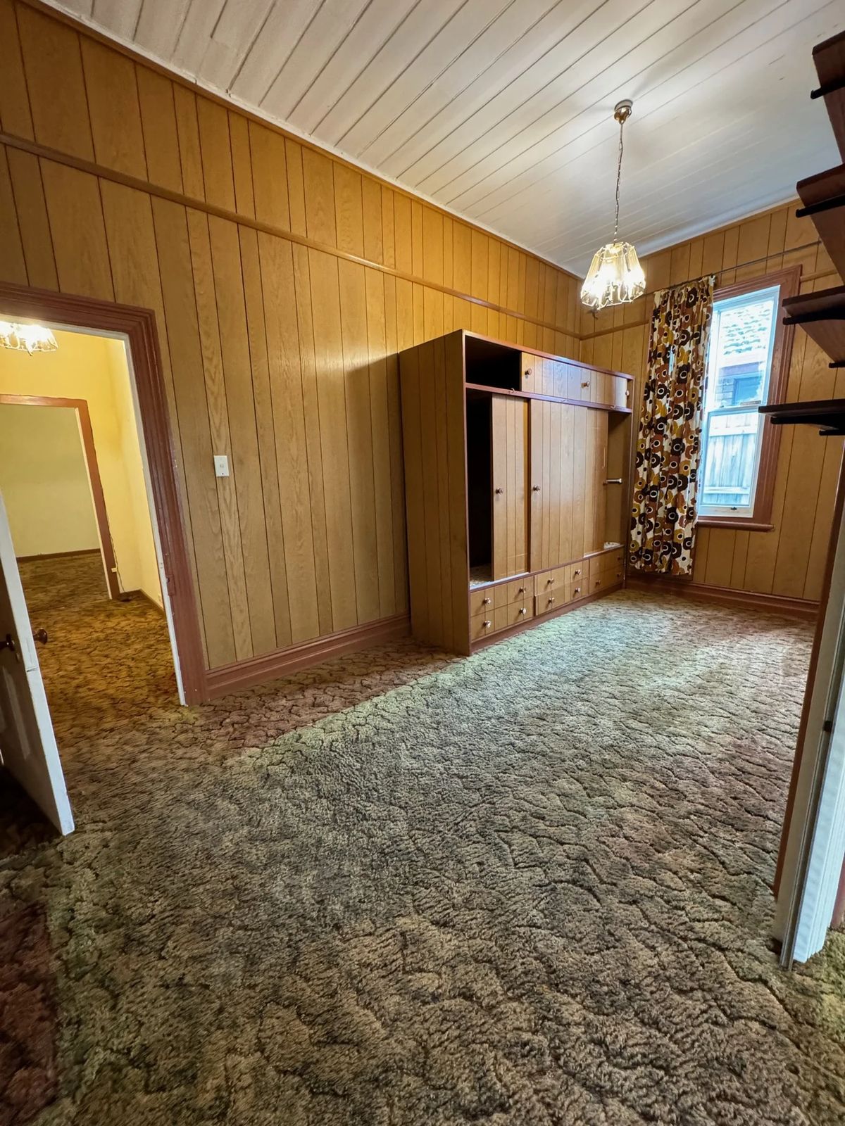 Lounge before with timber panelled walls and patterned carpet